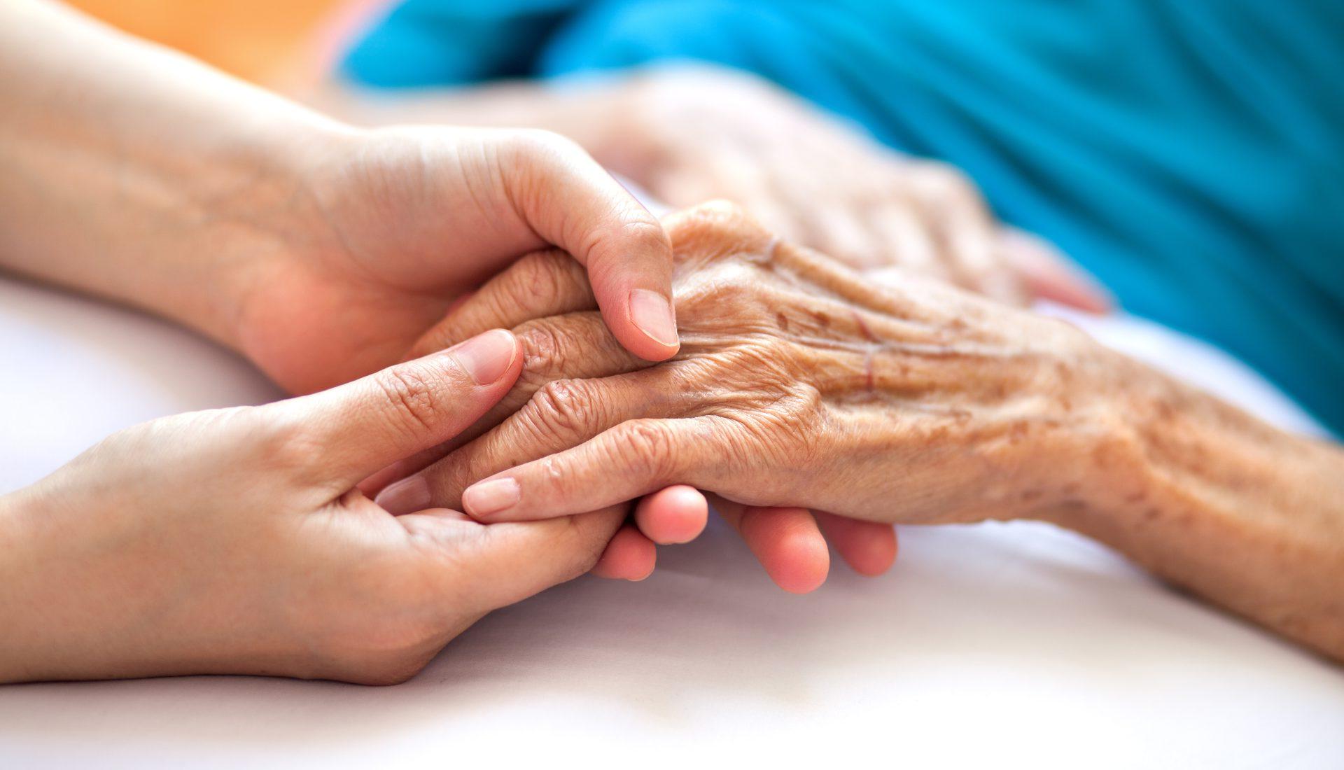 Woman holding senior woman's hand on bed